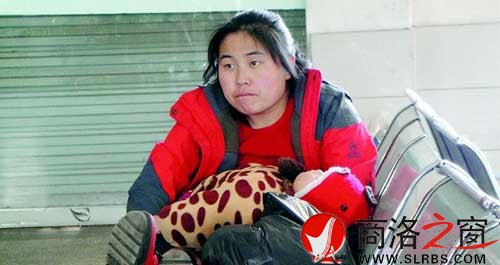 候車廳里，一位母親抱著睡著的孩子發(fā)呆